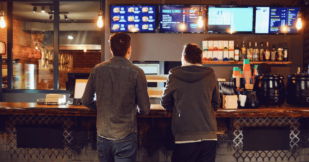 Two customers standing at a restaurant counter, illustrating the restaurant minimum wage discussion and its impact on hospitality operations