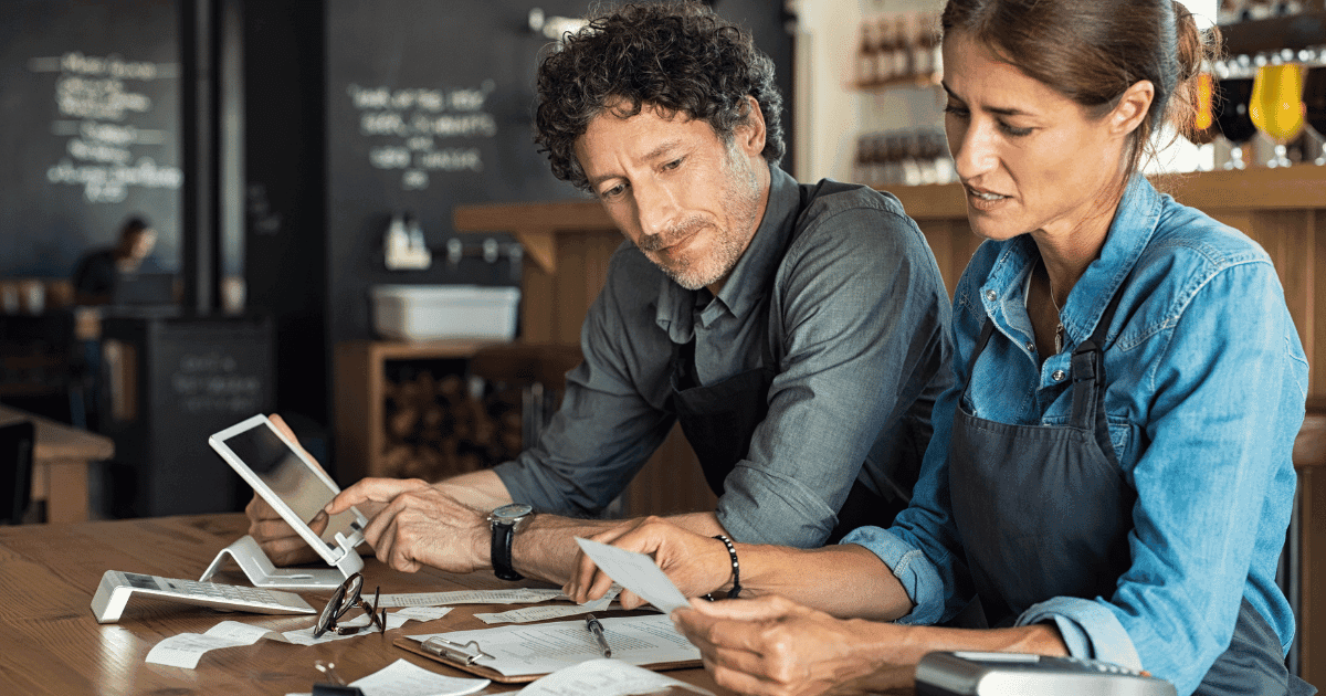 Two restaurant operators reviewing paperwork and hiring costs at a table, illustrating restaurant signing bonuses during the 2021 labor shortage