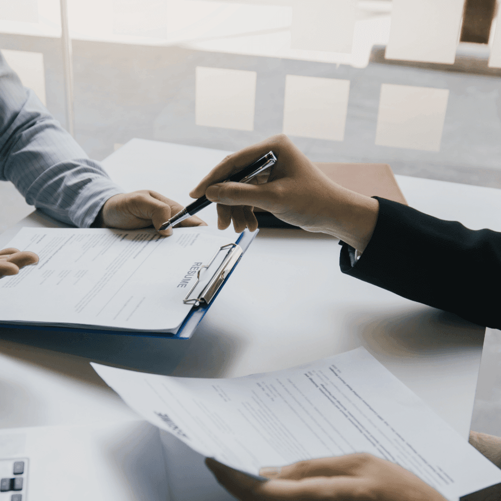 Two people at a desk reviewing a printed résumé on a clipboard